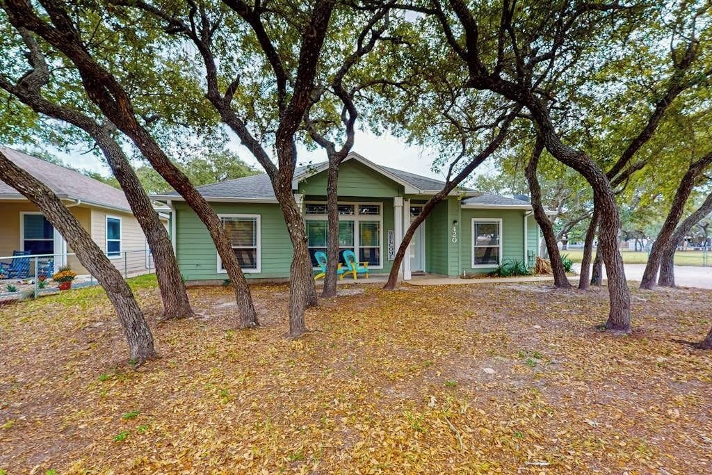 A single-story house with a green exterior, surrounded by trees and a leaf-covered ground.