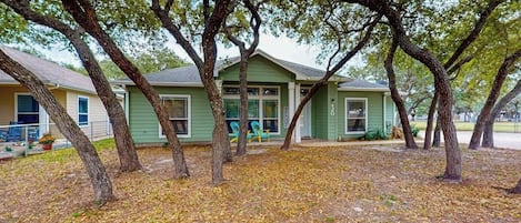 A single-story house with a green exterior, surrounded by trees and a leaf-covered ground.