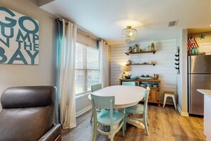A compact kitchen with a dining table, chairs, a refrigerator, and a decorative wall sign. - Beachaholic - Bay Views, Pool, Near the Beach (Rockport)