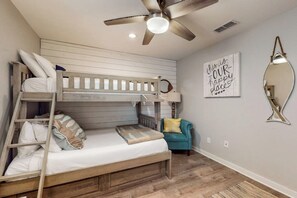Una cama litera con escalera, un ventilador de techo, una pared con espejo y una cita motivadora.