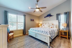 A bedroom with a bed, a ceiling fan, a nightstand, a lamp, a chair, and a fish decoration on the wall. - Beachaholic - Bay Views, Pool, Near the Beach (Rockport)