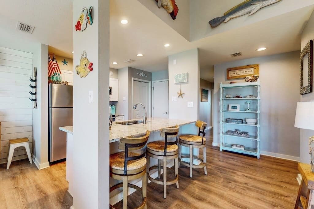 Una cocina con una isla central, taburetes de bar y un estante azul claro.