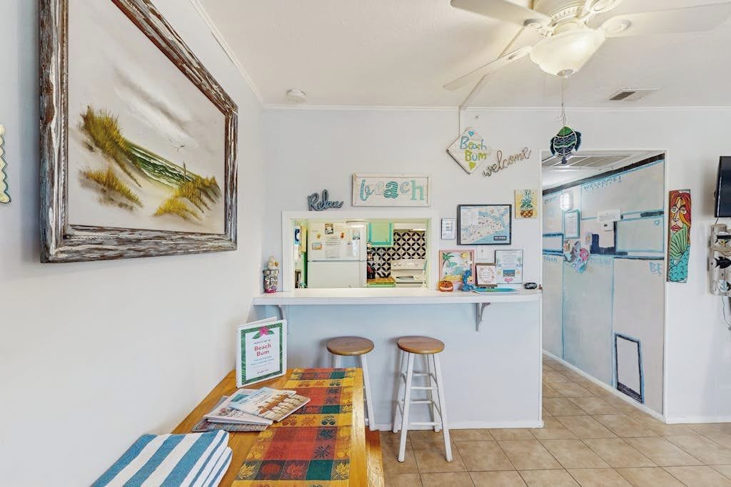 Un coin cuisine avec un plan de travail blanc, deux tabourets et un ventilateur de plafond.