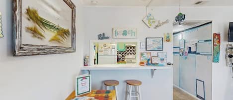 Un coin cuisine avec un plan de travail blanc, deux tabourets et un ventilateur de plafond.