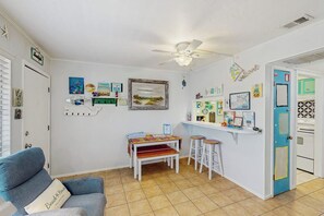 Ein Zimmer mit Deckenventilator, einer blauen Tür, einem kleinen Tisch mit Hocker und verschiedenen Wanddekorationen.