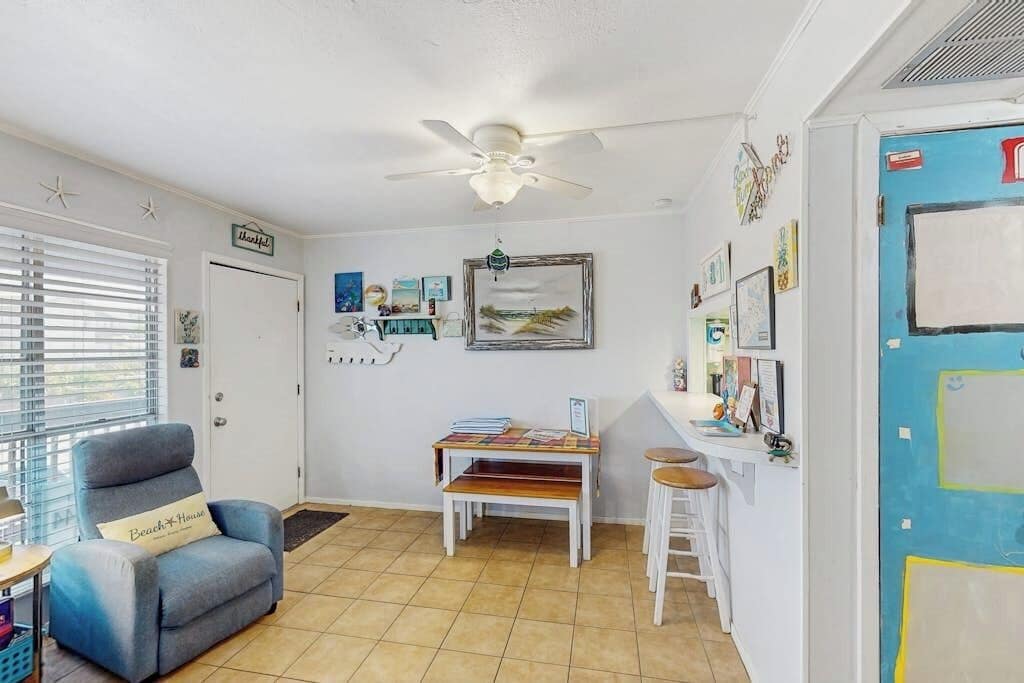 Une pièce dotée d’un ventilateur de plafond, d’un bureau avec une chaise, d’une petite table avec un banc et d’une porte ornée d’œuvres d’art.