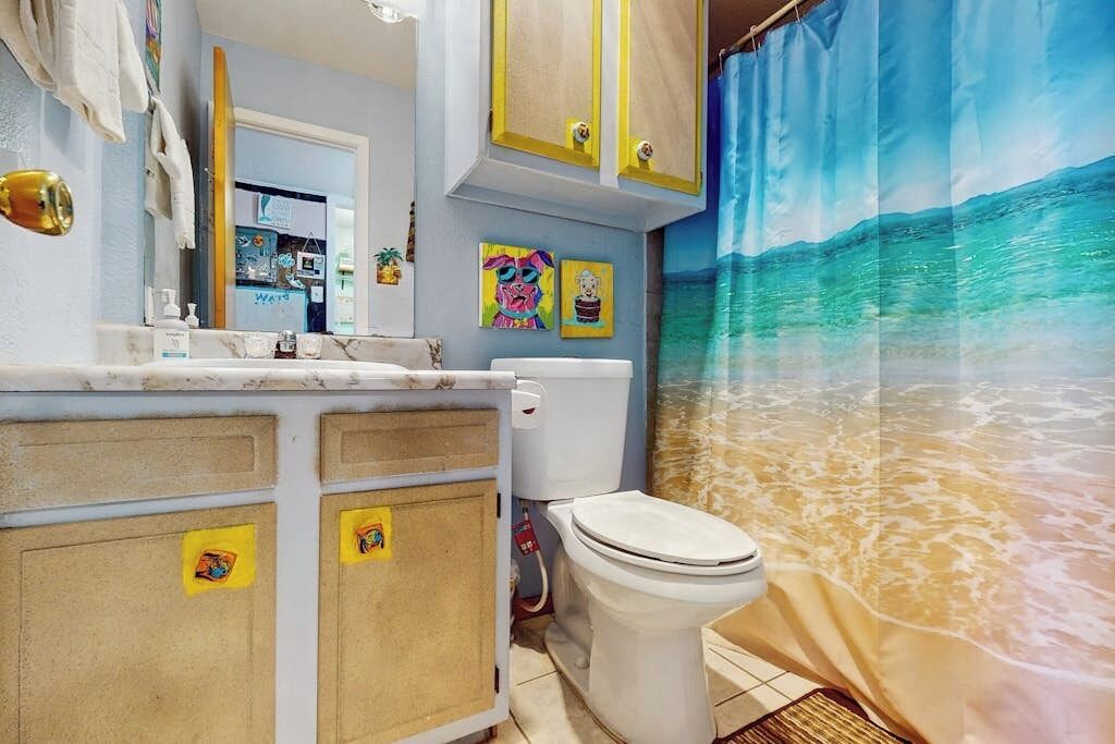A bathroom with a toilet, a sink, and a shower curtain depicting a beach scene.