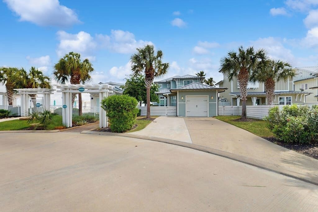A residential area with houses, a gated entrance, and palm trees.