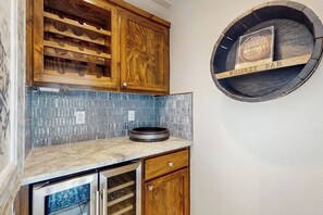 A kitchen with wooden cabinets, a blue tiled backsplash, a marble countertop, and a whiskey bar sign. - Saltwater Serenity at the Reserve (Rockport)