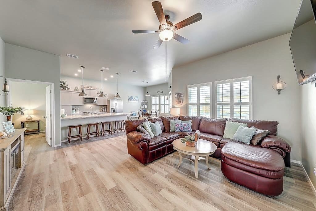 A spacious living room with a leather sofa, a coffee table, and a ceiling fan.