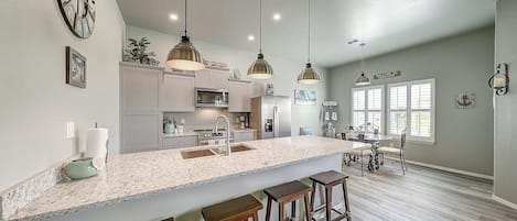 Cozinha com ilha central, banquetas, iluminação pendente e área de jantar com mesa e cadeiras.