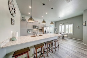 A kitchen with a central island, bar stools, pendant lighting, and a dining area with a table and chairs. - Sea La Vie on Paradise (Rockport)