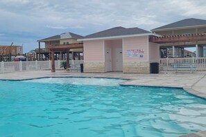Zona de piscina amb un edifici a prop, una tanca de palets blancs i un cel serè.