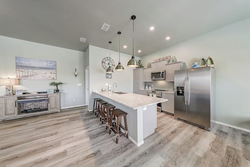 A modern kitchen with a central island, bar stools, stainless steel appliances, and pendant lighting.