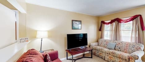 A living room with a red sofa, a floral-patterned sofa, a flat-screen TV, and a lamp.
