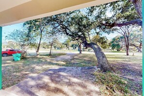 An outdoor area with trees, a paved path, and a red vehicle. - The Bay Breeze - Single-Level with Large Yard (Aransas Pass)