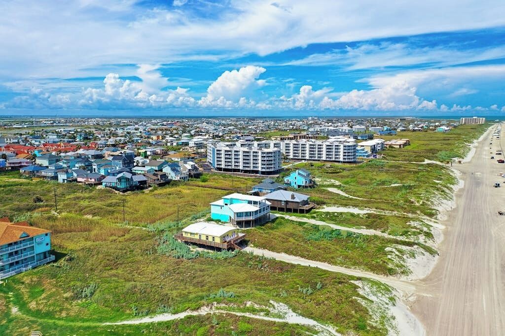A coastal town with beachfront properties, a main road, and a clear sky.