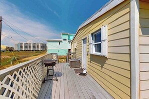 A wooden deck with a white fence, a small table, and a window. - Shore Thing - Gulf-Front, 65 Steps to Beach (Port Aransas)