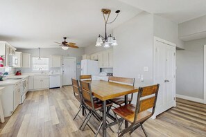 A modern kitchen with white cabinetry, a wooden dining table, and a ceiling fan. - Shore Thing - Gulf-Front, 65 Steps to Beach (Port Aransas)