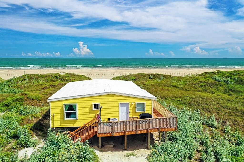 A yellow beach house with a wooden deck and a staircase leading to a covered porch.