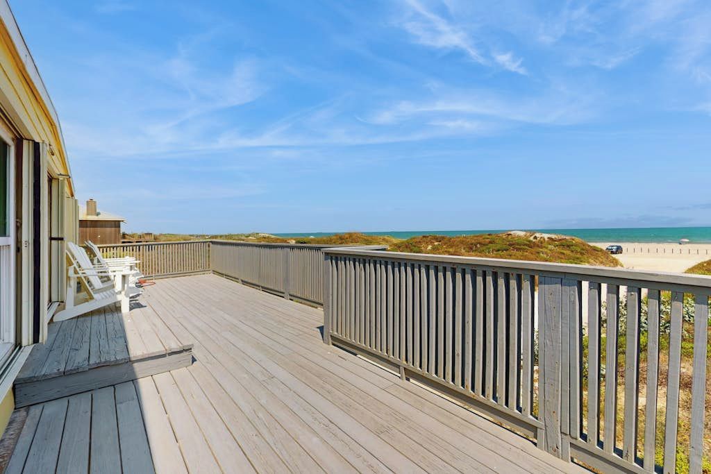 A wooden deck with a railing, overlooking a beach and ocean.