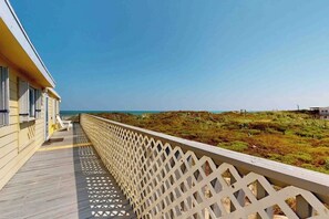 Eine Holzterrasse mit Gittergeländer und Blick auf einen Strand.