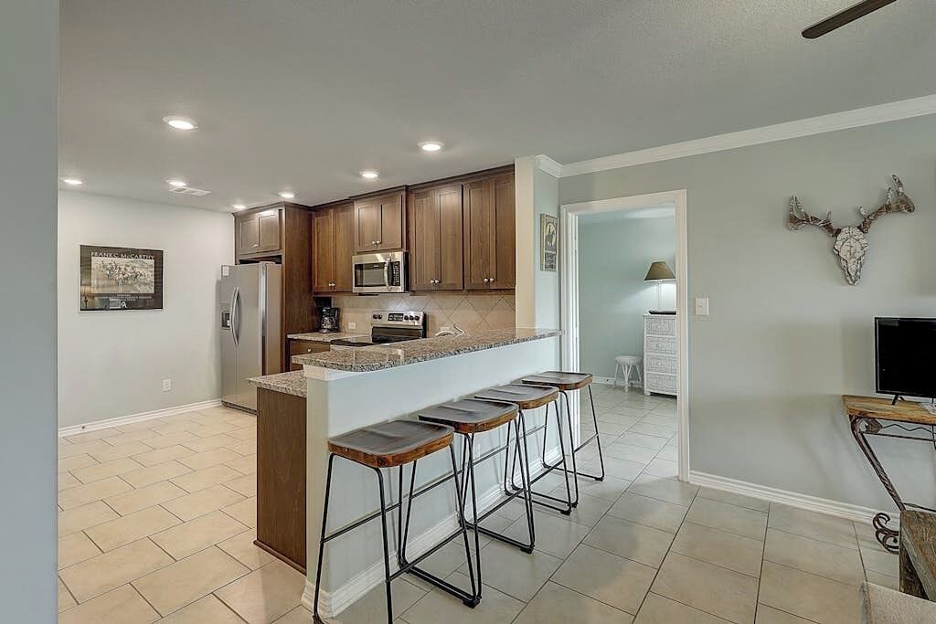 A kitchen with wooden cabinets, a microwave, and a bar area with stools.