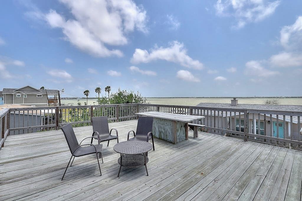 Eine Holzterrasse mit Gartenmöbeln, Blick auf den Strand und ein Boot in der Ferne.