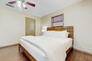 Ein Schlafzimmer mit einem hölzernen Bett, einem Deckenventilator, einem Fenster mit Jalousien und einer Tür.