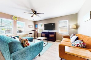 Ein Wohnzimmer mit einer Couch, Sesseln, Fernseher, Deckenventilator und einem Schrank.