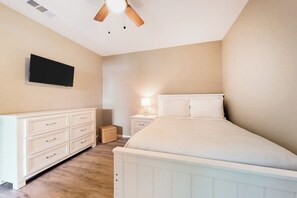 Quarto com cama, cômoda, mesa de cabeceira, abajur e ventilador de teto.