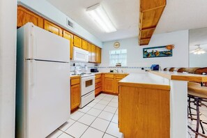 A kitchen with wooden cabinets, a white refrigerator, a stove, and a large island with bar stools. - Casa de la Isla/Mars Island Unit A (South Padre Island)