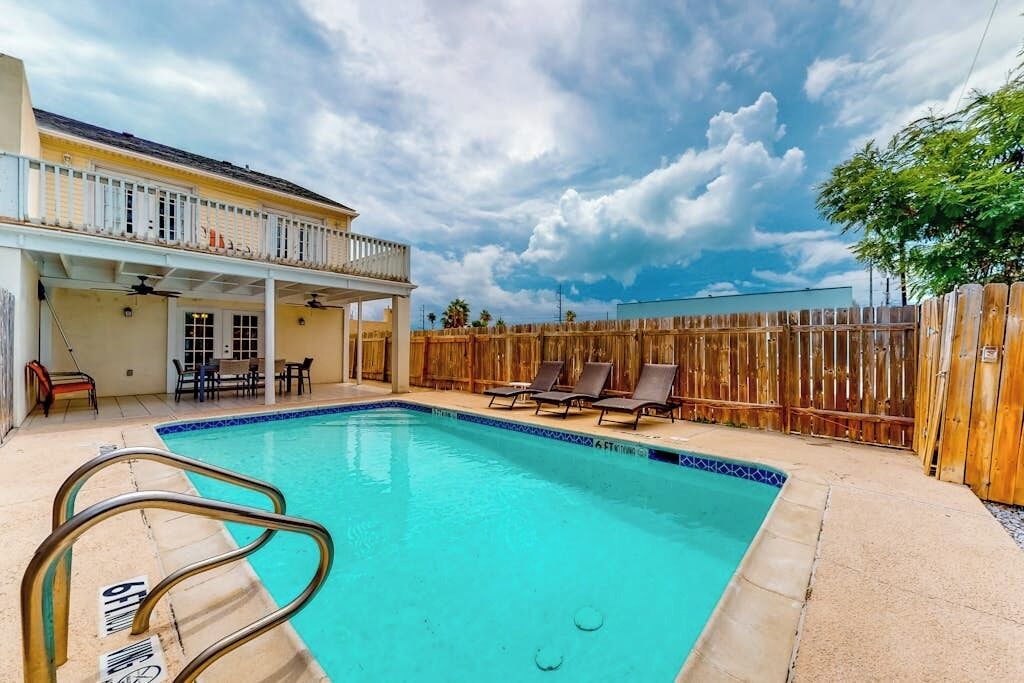 Ein Schwimmbad mit Holzumzäunung, Liegestühlen und einer überdachten Terrasse.