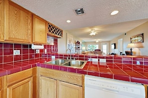 A kitchen with wooden cabinets, a red tiled backsplash, a built-in dishwasher, and a ceiling fan. - Suntide II Condominiums #308 (South Padre Island)