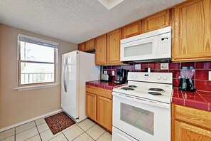 A kitchen with wooden cabinets, a white refrigerator, a microwave, a stove, and a red tiled backsplash. - Suntide II Condominiums #308 (South Padre Island)