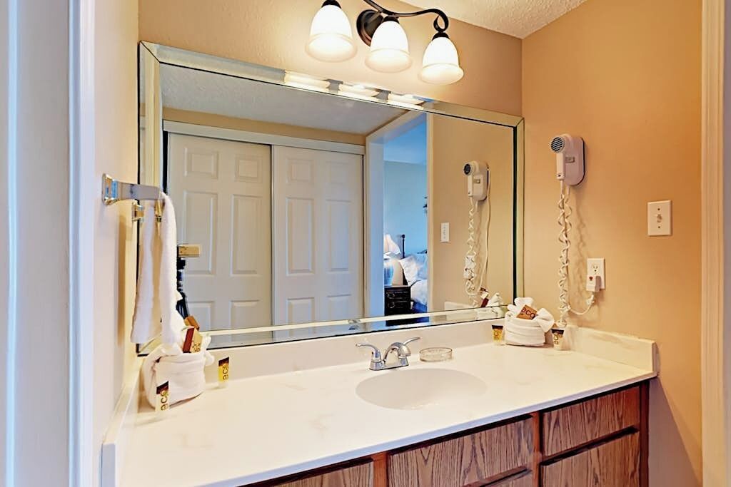 Une salle de bain avec un grand miroir, un lavabo, un porte-serviettes et un sèche-cheveux fixé au mur.