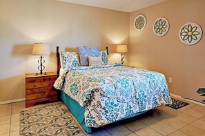 A bedroom with a bed, two bedside tables, a nightstand, and a patterned rug. - Suntide II Condominiums #308 (South Padre Island)
