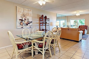 A dining area with a glass table and white chairs, a sofa, and a bookshelf. - Suntide II Condominiums #308 (South Padre Island)