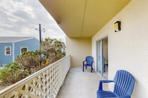 Ein Balkon mit einem weißen Gittergeländer, zwei blauen Stühlen und einer Glastür, die zu einem Innenraum führt.
