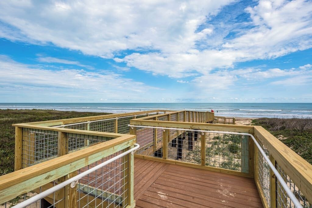 A wooden deck with a metal railing overlooking a beach.