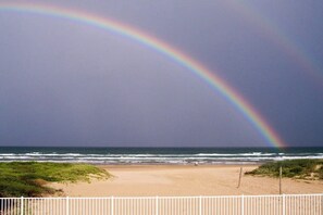 A beach with a white fence and a rainbow in the sky. - Fiesta Sol Condominiums 211 (South Padre Island)