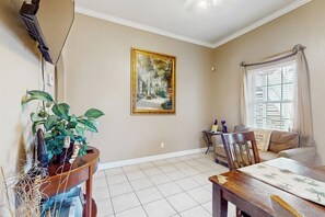 Een woonkamer met een eettafel, een bank, een schilderij aan de muur en een raam met gordijnen.