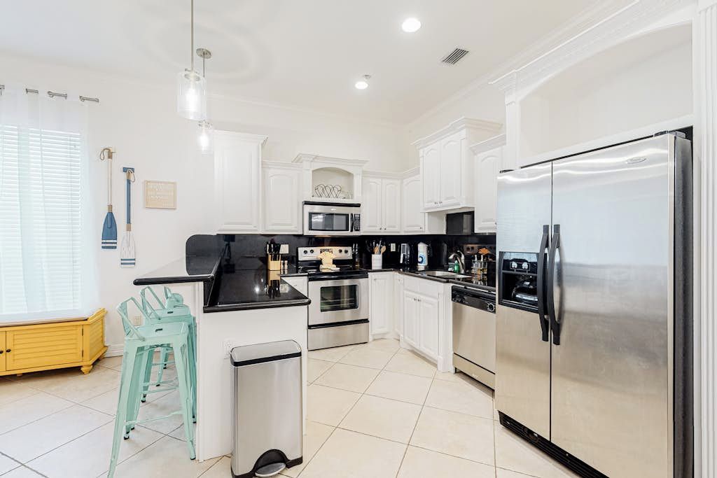 A modern kitchen with white cabinetry, stainless steel appliances, and a teal bar stool.