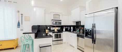 A modern kitchen with white cabinetry, stainless steel appliances, and a teal bar stool.