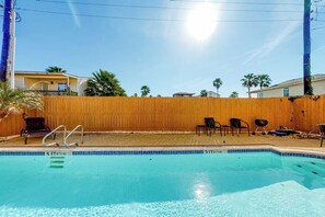 A swimming pool with a wooden fence, lounge chairs, and a clear blue sky. - Las Palmas de Acapulco #2 (South Padre Island)