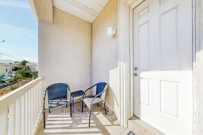 A balcony with two chairs and a small table, a white door, and a view of the neighborhood. - Las Palmas de Acapulco #2 (South Padre Island)