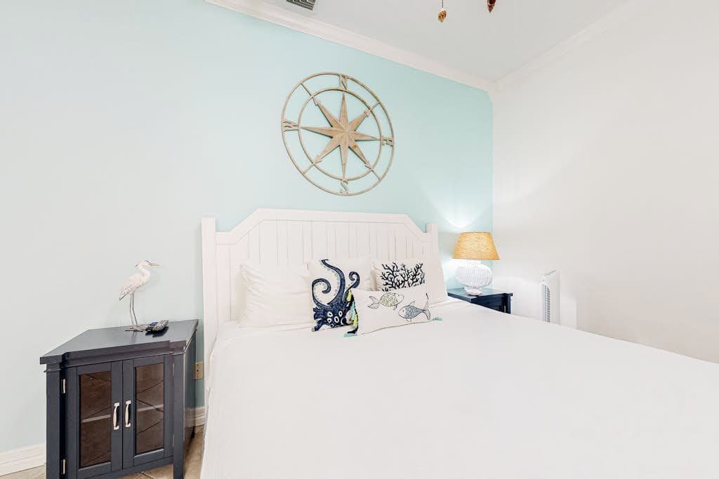 A bedroom with a bed, a nightstand, a wall-mounted compass, and a lamp.