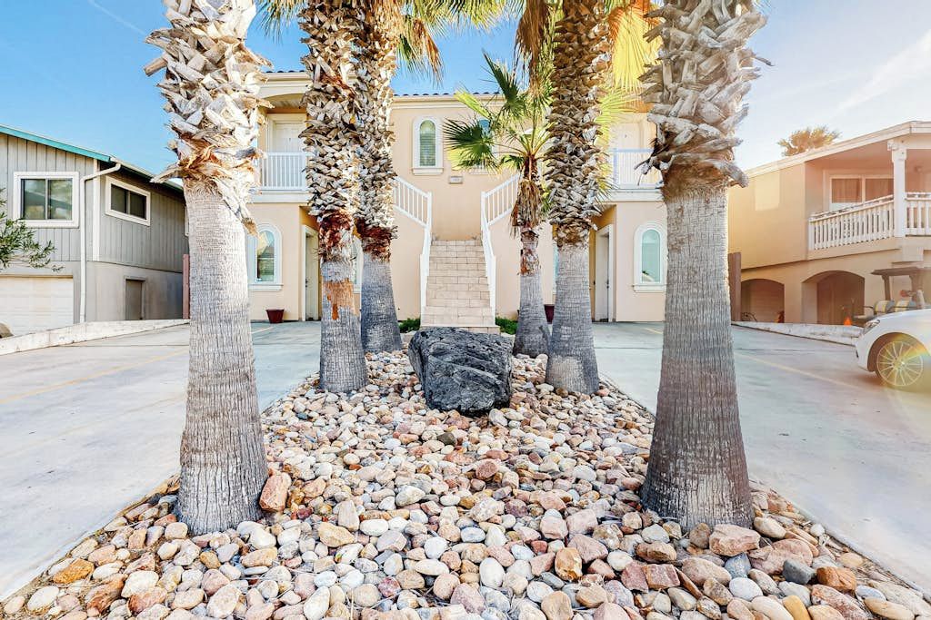 Un patio con palmeras, un sendero de piedra y un edificio con balcón.