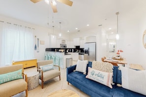 A modern living room with a blue sofa, a wooden coffee table, and a kitchen area with white cabinets and stainless steel appliances. - Las Palmas de Acapulco #2 (South Padre Island)