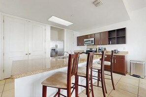 Cozinha moderna com ilha central, eletrodomésticos de aço inoxidável e banquetas de madeira.